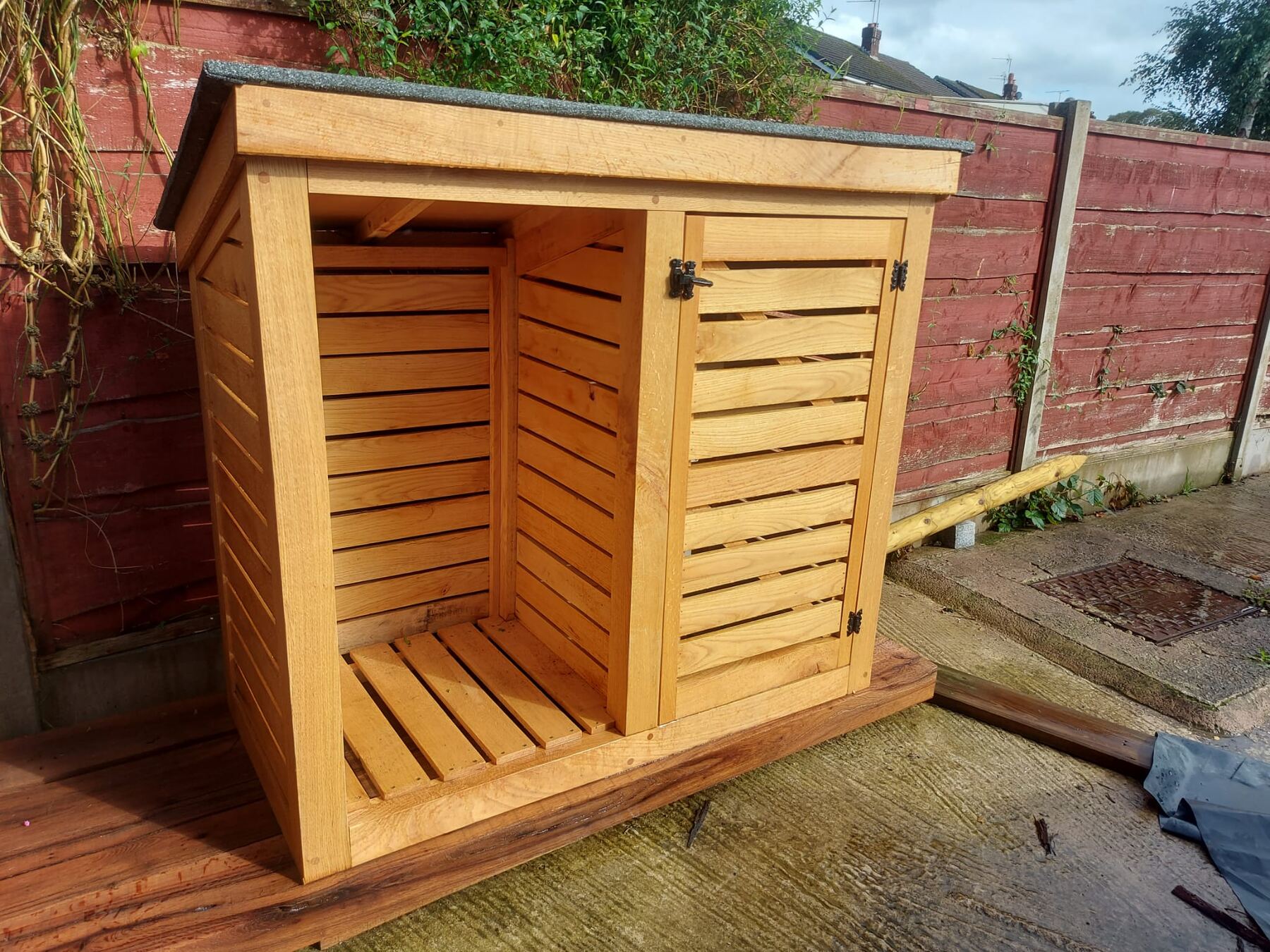 Slatted solid oak log store beside a garden fence